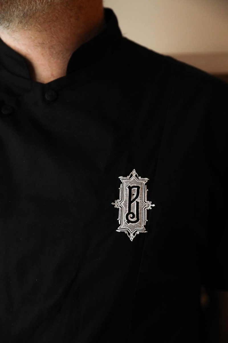logo argenté de la Boulangerie Baptiste sur un veste de cuisine noire