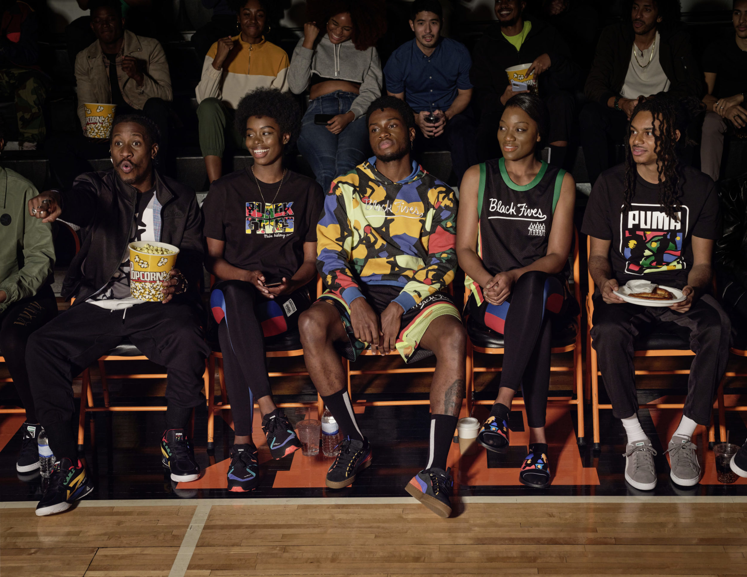 la black five foundation mise en avant, trois jeunes noires regardent un match de basket-ball, une fille parmi eux, tous les spectateurs sont noirs et le pop-corn est au rendez-vous