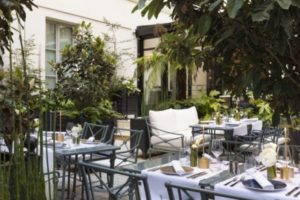 terrasse avec des palmiers verts, des chaises et des tables garnis de coupes de vins et d'assiettes de porcelaine