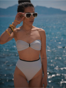 leeloo avec des lunettes de soleil et la plage derrière elle avec un bikini blanc