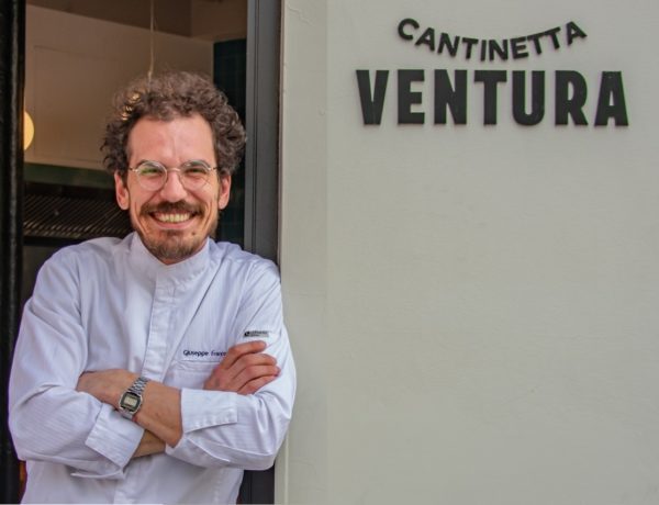 serge ventura, moustachu châtain bouclé, adossé à l'enseigne de son restaurant Cantinetta Ventura