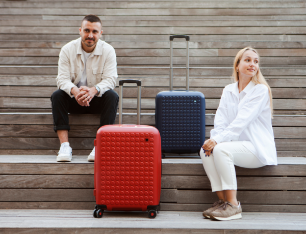 Dot-Drops : un homme et une femme regarde autour d'eux assis sur des escalier avec une valise rouge et une valise bleue marine à leur côté