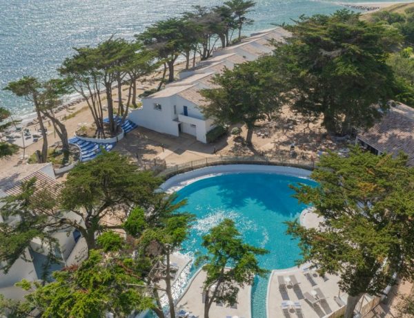 Prise de vue de l'hotel. Piscine visible, entourée des arbres.
