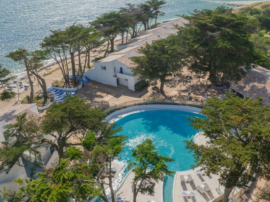 Prise de vue de l'hotel. Piscine visible, entourée des arbres.
