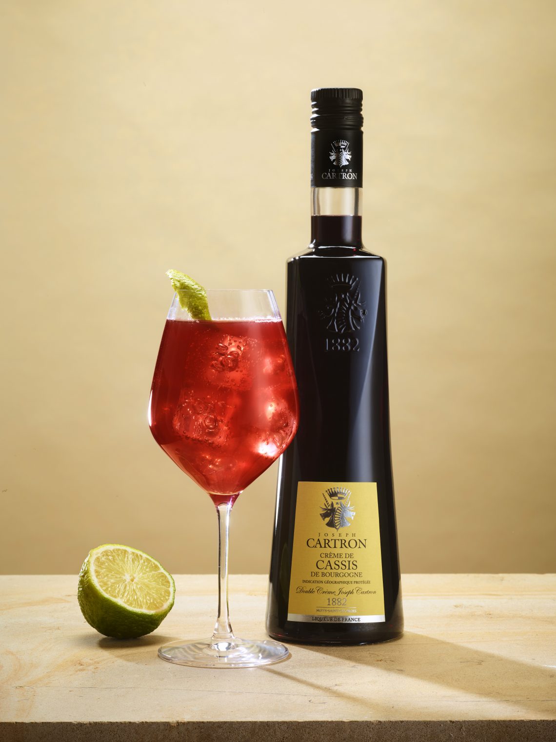 Cocktail avec la bouteille de cassis à côté et un citron vert.