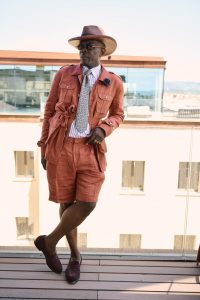 Homme portant une saharienne et un bermuda en lin terracotta avec chapeau et loafers, look d’été Hockerty au Pitti Uomo 108.