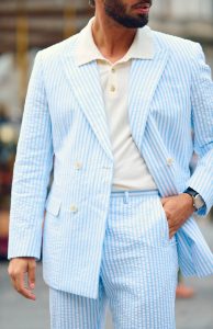 Homme portant un costume croisé en seersucker bleu clair et chemise polo beige, look estival Hockerty au Pitti Uomo Été 2025.