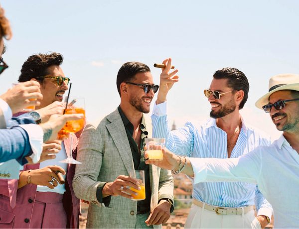 Groupe d’hommes élégants en costumes d’été Hockerty trinquant sur un rooftop à Florence pendant le Pitti Uomo 108.
