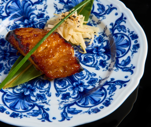Plat signature japonais chez UNI Paris, poisson laqué servi sur une assiette en porcelaine bleue.