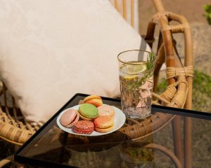 assiette de macarons de Franck Deville avec un verre de boissons sur table en verre et chaise en bois