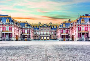 Le Chateau de Versailles de face, au couché de Soleil en arrière plan, ciel bleu dégradant orange