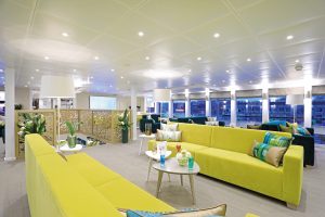 Photo prise à l'intérieur du bateau de croisière. Canapé vert clair et foncé, baie vitré avec un paysage de ville parisienne.